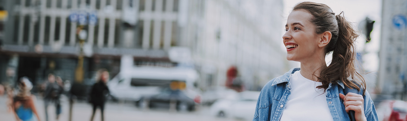 A young woman in a cityscape, smiling and looking to the side.