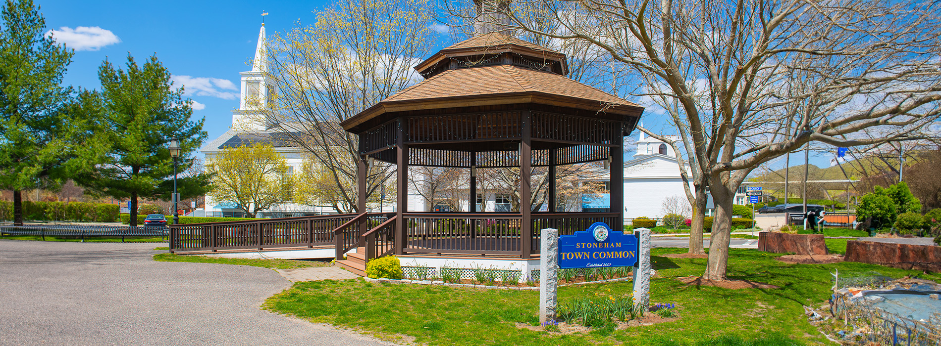 The image shows a picturesque scene with a prominent gazebo, a blue sign with white text in the background, and a clear sky.