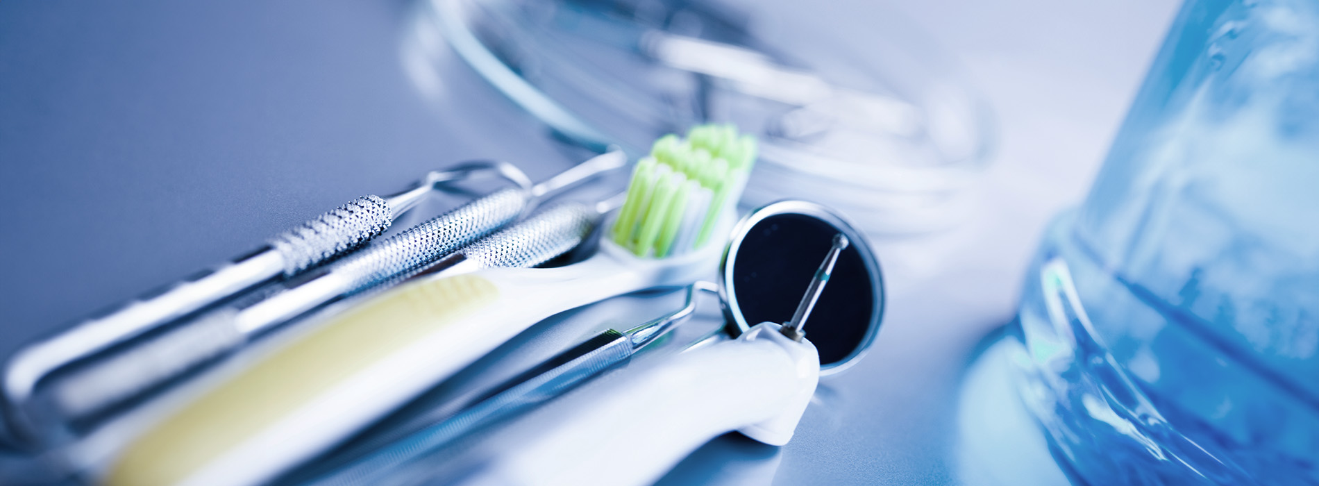 The image shows a collection of medical instruments and equipment, including scissors, forceps, and other tools commonly found in a dental or surgical setting, arranged on a table with a blue water bottle and a clear plastic container in the foreground.