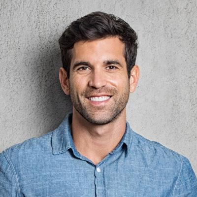 A man with a beard and mustache is smiling at the camera, posing against a gray background.