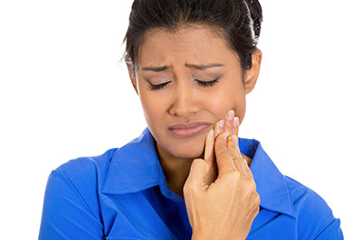 A woman with a concerned expression, looking down at her hand holding a small object that appears to be a toothbrush or dental tool.