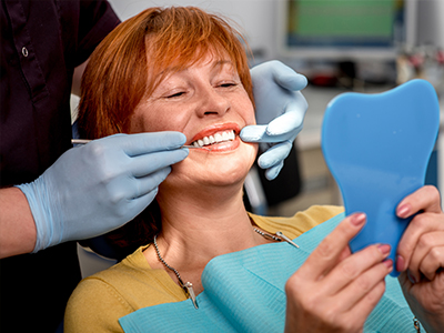 A woman in a dental chair receiving dental care, with a dental professional adjusting her mouthpiece.