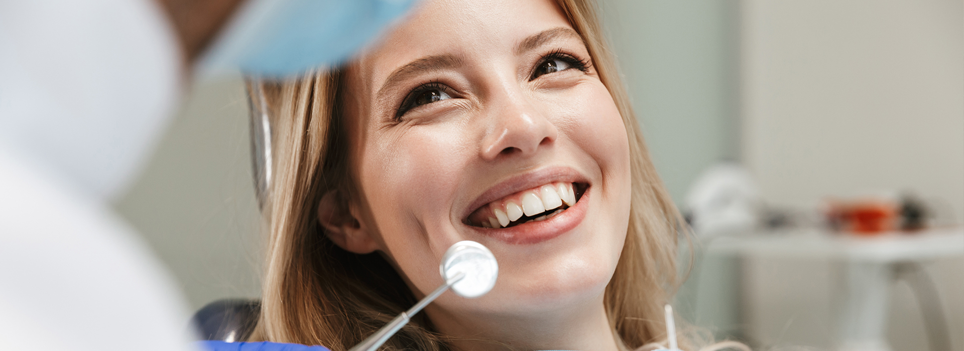 A woman is smiling in a dental office while sitting in the dentist s chair, with a dental professional attending to her.