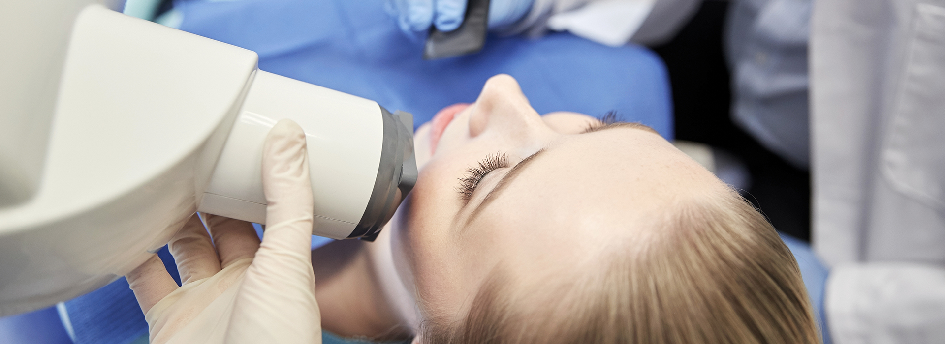 The image shows a woman in a medical setting, receiving treatment or examination with a device that appears to be a dental or oral care instrument.