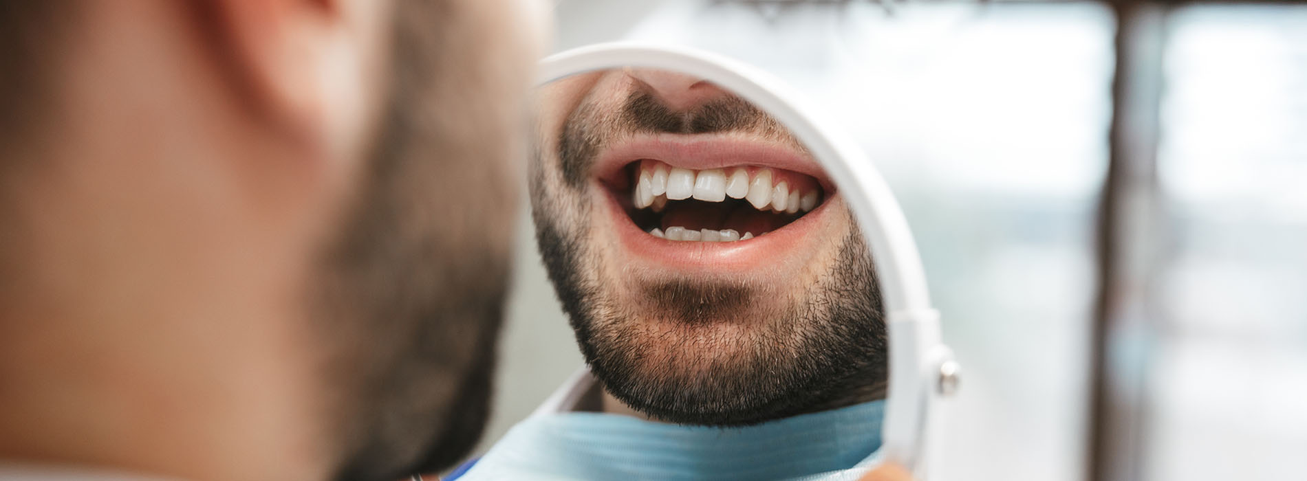 An image of a man with a beard and mustache smiling at the camera, showing his teeth, with a blurred background that suggests an indoor setting.