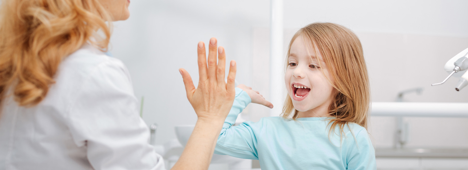 The image is a photograph of a woman and a young girl in a bathroom, with the woman standing behind the child who is sitting on a chair. The woman appears to be interacting with the child, possibly engaging in an activity or conversation.