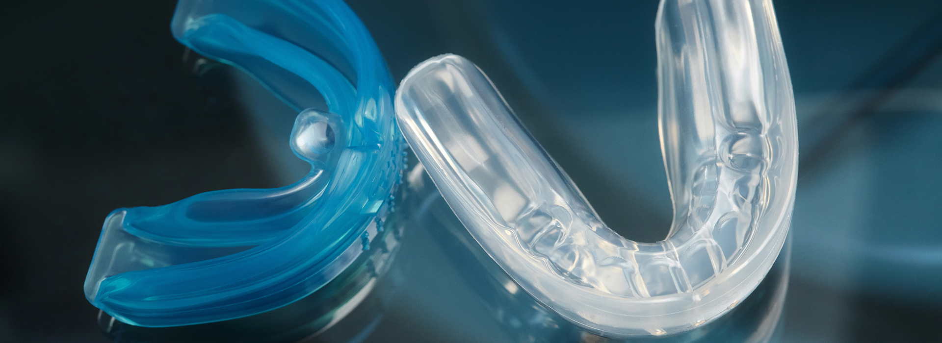 The image shows a blue and clear plastic toothbrush with bristles, set against a blurred background.