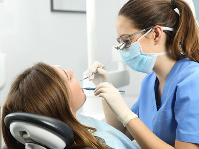 Woman in blue scrubs performing dental procedure on patient.