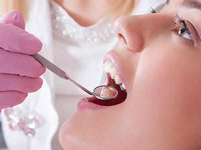A woman in a dental office receiving dental care, with a dentist using a device to examine her teeth.