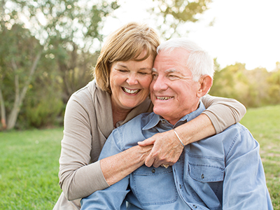 An elderly couple embracing, with the woman wearing a white top and glasses, and the man in a blue shirt.