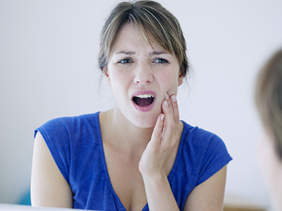 The image shows a woman with her mouth open, possibly in the middle of speaking or singing. She appears to be indoors and is looking at her own reflection in a mirror.