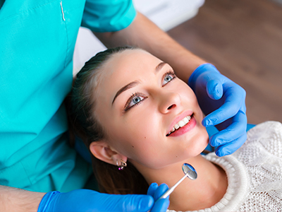 A dental hygienist is performing a teeth cleaning procedure on a woman, with the woman smiling and looking upwards.