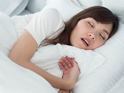 A woman is lying in bed, with her eyes closed and a peaceful expression on her face.