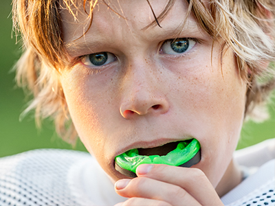 A young male athlete with blonde hair, wearing a football uniform and holding a green toothbrush to his mouth.