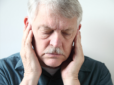 The image features an elderly man with a mustache, wearing glasses and holding his hand to his ear. He appears to be in a state of discomfort or pain.