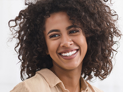 The image shows a smiling person with curly hair, wearing a light-colored top and looking directly at the camera.